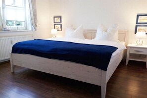 A single-bed room with a white frame, a blue bedspread, two bedside tables with lamps, and a window with curtains. - 2 in the Granitz house (Binz)