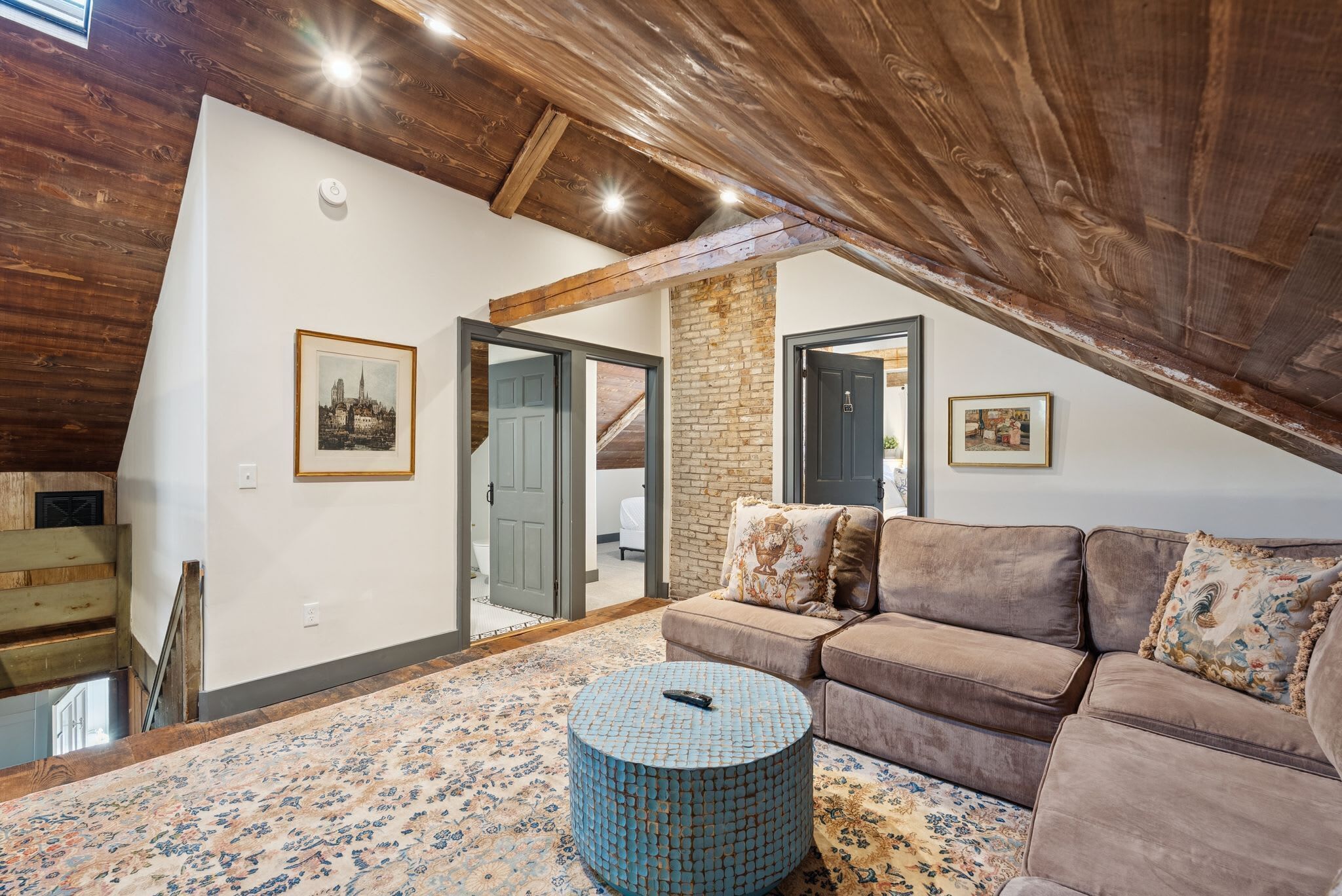 An attic room with a brown leather sofa, a patterned rug, and a blue mosaic coffee table.