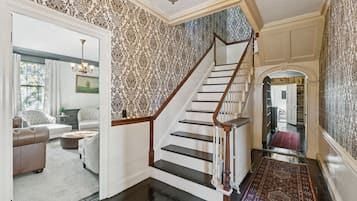 A staircase with a wooden handrail and black steps, leading to a room with patterned wallpaper and a chandelier.