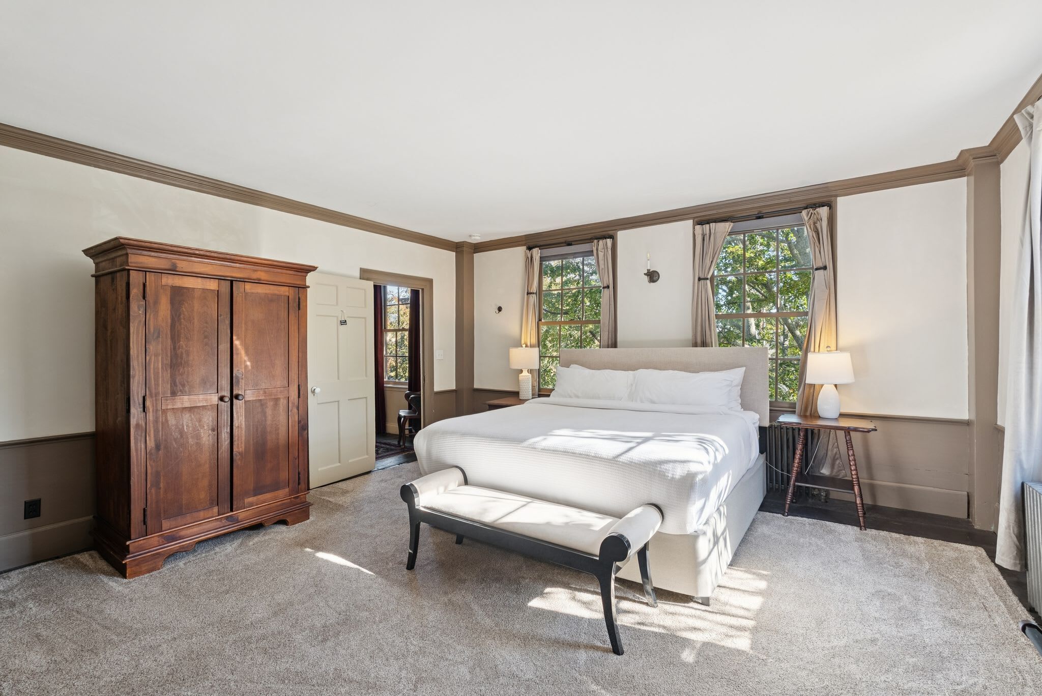A bedroom with a large bed, a wooden wardrobe, and a bench.