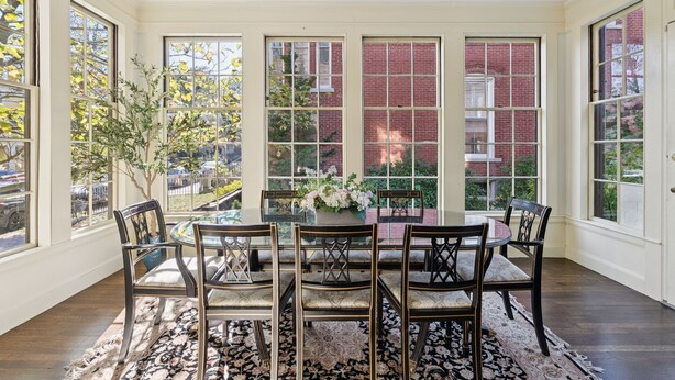 A dining area with a round table, six chairs, and a floral centerpiece.