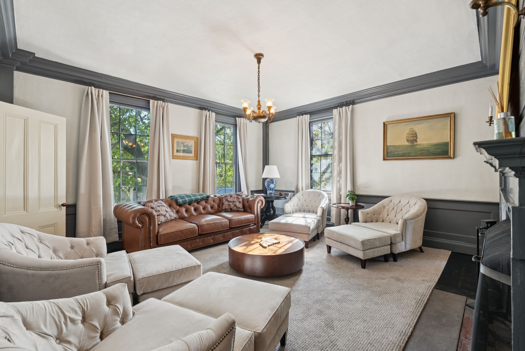 A spacious living room with a brown leather sofa, beige armchairs, and a round coffee table.