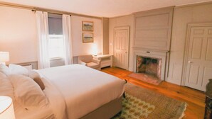A bedroom with a large bed, a chair, a fireplace, and a door.