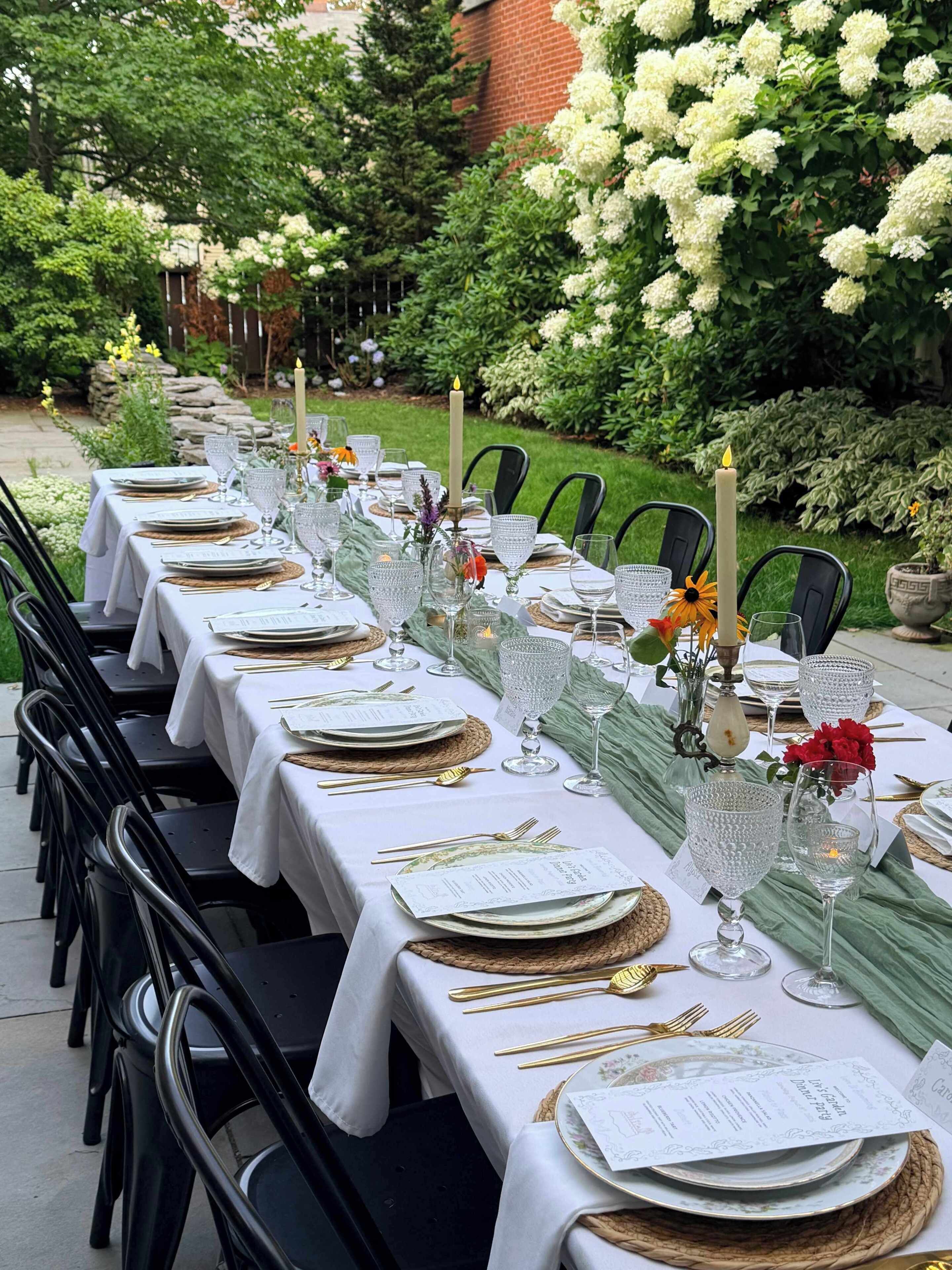An outdoor dining area with tables set for a meal, featuring white tablecloths, glassware, and candles.