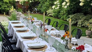 An outdoor dining area with tables set for a meal, featuring white tablecloths, glassware, and candles.