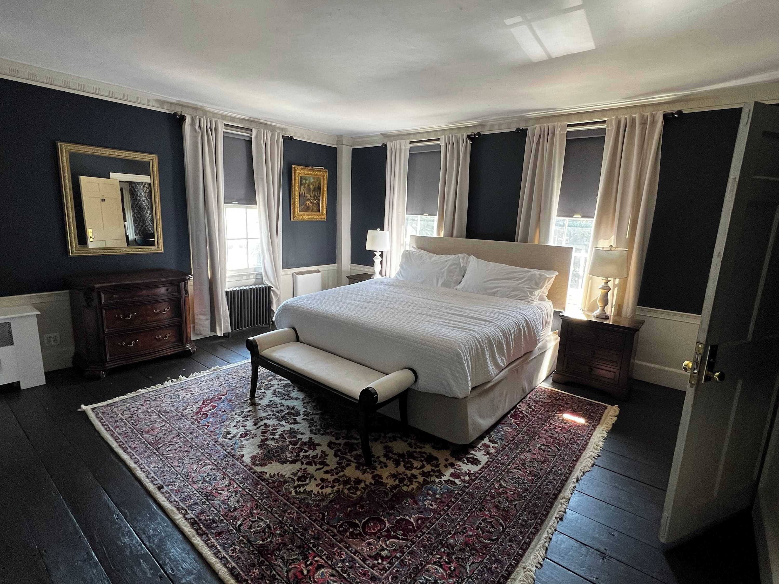 A bedroom with a large bed, a bench, a dresser, and a patterned rug.
