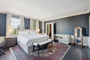 A bedroom with a large bed, a bedside table, a chair, a mirror, and a window with curtains. - Experience the History of Portland - The Hope Island Room (Portland)