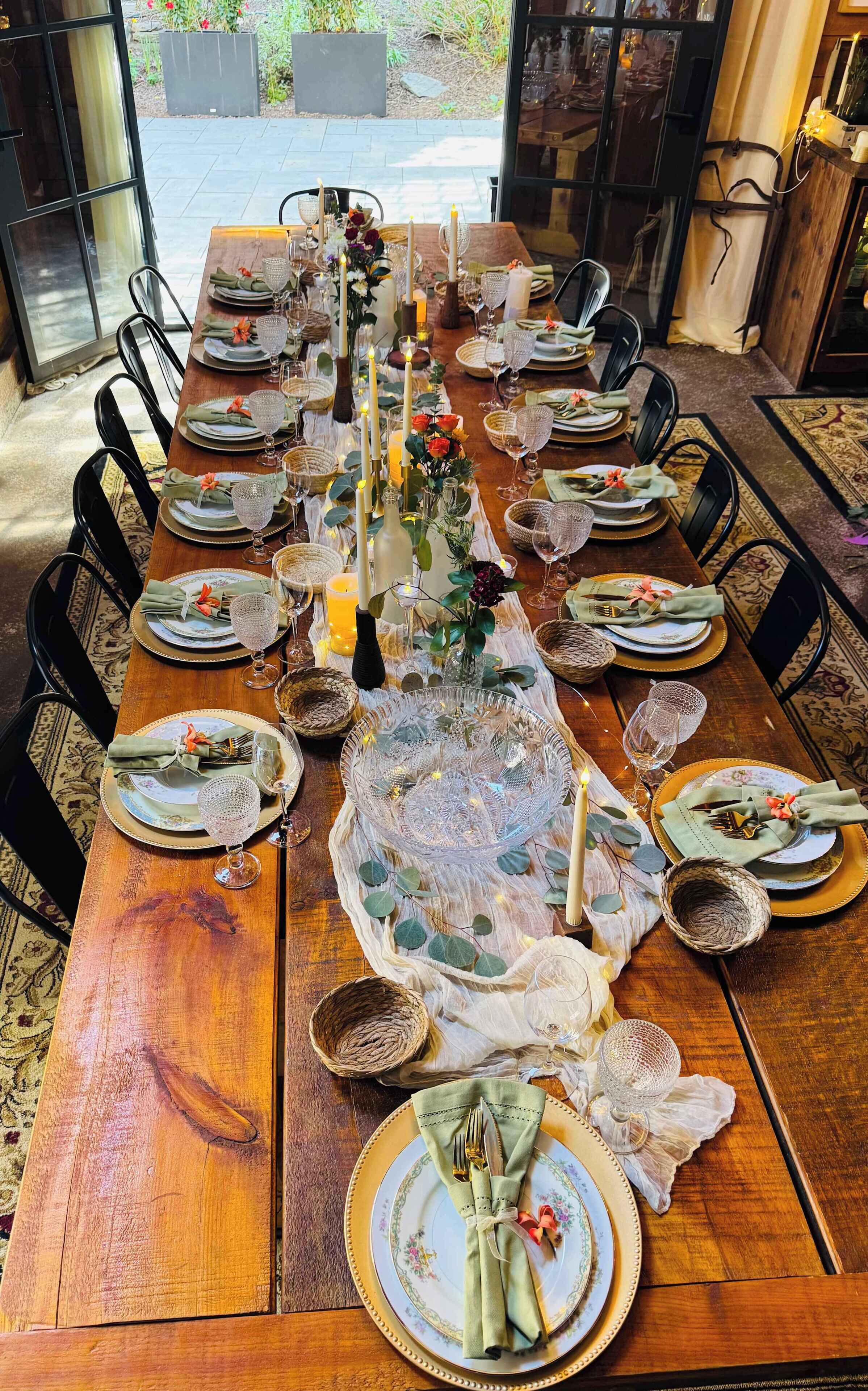 A long dining table set for a meal with multiple chairs, candles, and decorative centerpieces.