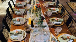 A long dining table set for a meal with multiple chairs, candles, and decorative centerpieces.