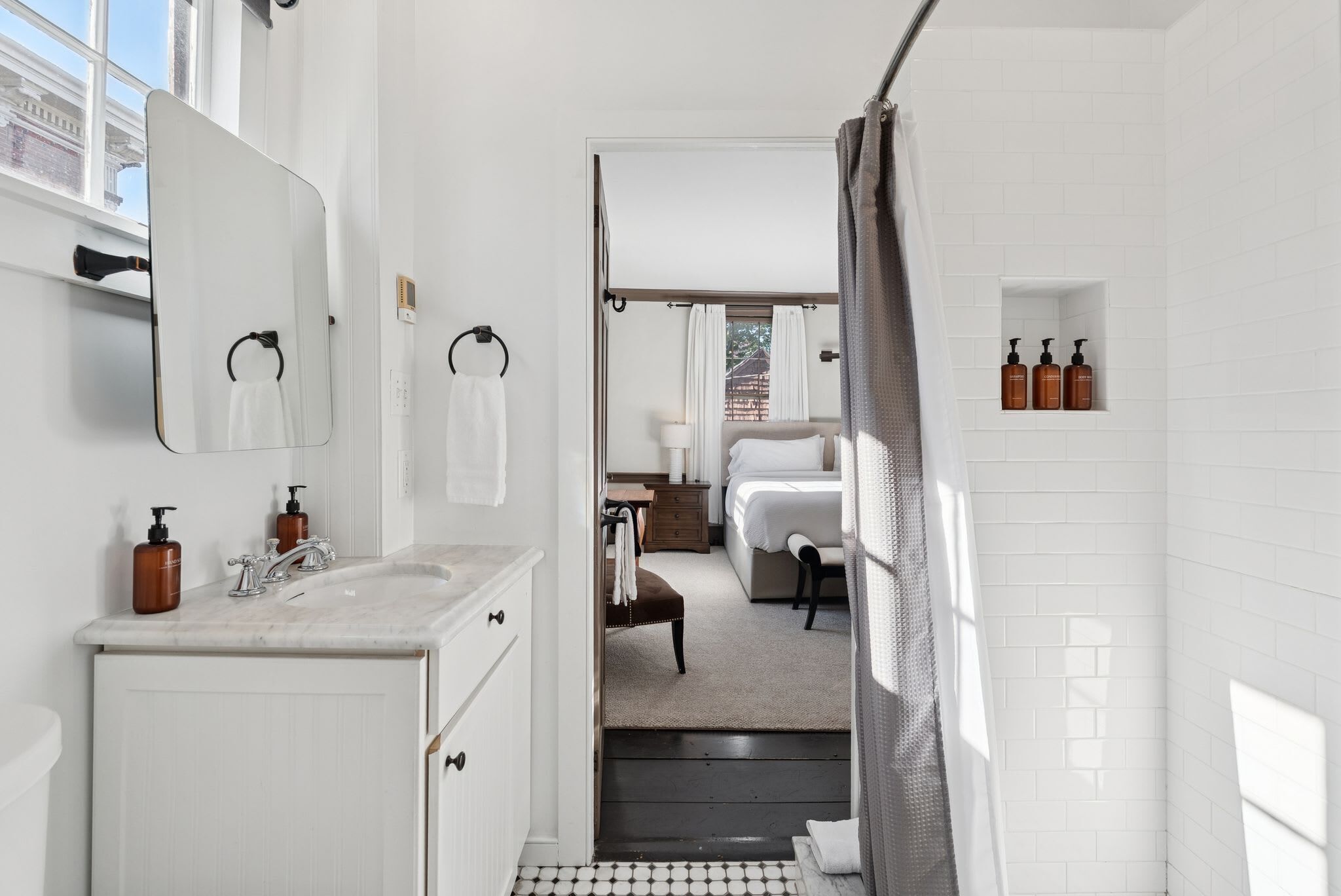 A modern bathroom with a large mirror, a sink with soap dispensers, a shower area, and a view of the outside.