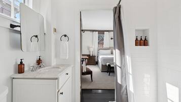 A modern bathroom with a large mirror, a sink with soap dispensers, a shower area, and a view of the outside.