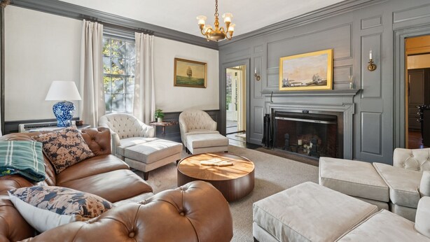 A living room with a fireplace, leather sofa, and a chandelier.