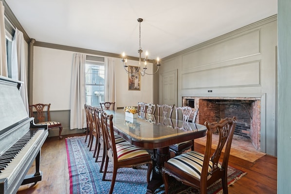 A dining room with a piano, a chandelier, and a fireplace.