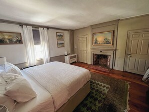 A hotel room with a bed, a fireplace, a door, and a painting on the wall.