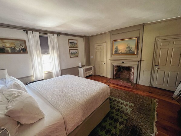 A hotel room with a bed, a fireplace, a door, and a painting on the wall. - Experience the History of Portland - The Hope Island Room (Portland)
