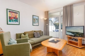 A living room with a sofa, a coffee table, a television, and artwork on the walls. - 03, Residence Dünenstraße (Binz)