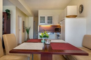 A compact kitchen with white cabinets, a microwave, and a refrigerator. There is a dining table with two chairs and a vase of flowers. - Dream time at Villa Freia (Binz)