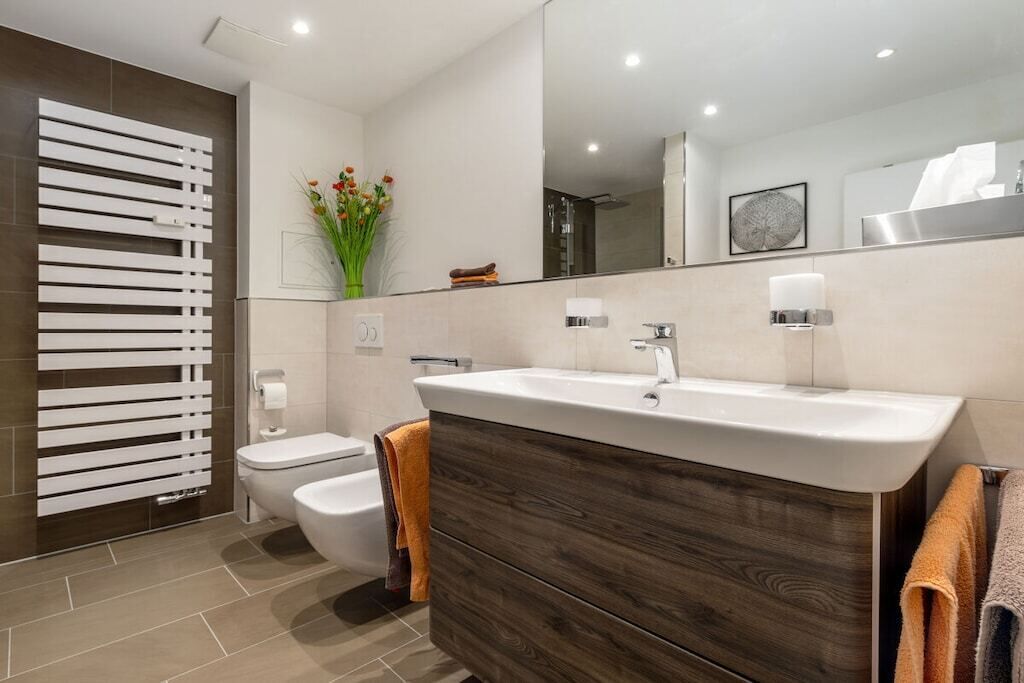 A modern bathroom with a large mirror, a wooden vanity, a toilet, and a towel rack.