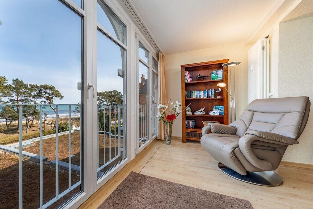 Une pièce dotée d’une grande porte-fenêtre coulissante donnant sur un balcon avec vue sur la plage. On y trouve également une bibliothèque et un fauteuil inclinable.
