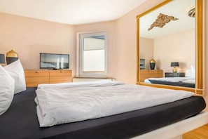 Ein Hotelzimmer mit einem Bett, einem Fernseher, einem Schminktisch, einem Spiegel und einem Fenster.