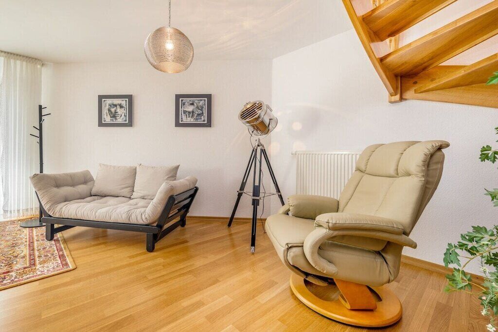 Una sala moderna con un sofá, un sillón reclinable, una lámpara de pie y una luz sobre trípode.
