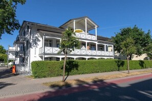 Ein zweistöckiges Gebäude mit einem Balkon, einer überdachten Außen-Sitzgelegenheit und blauem Himmel.