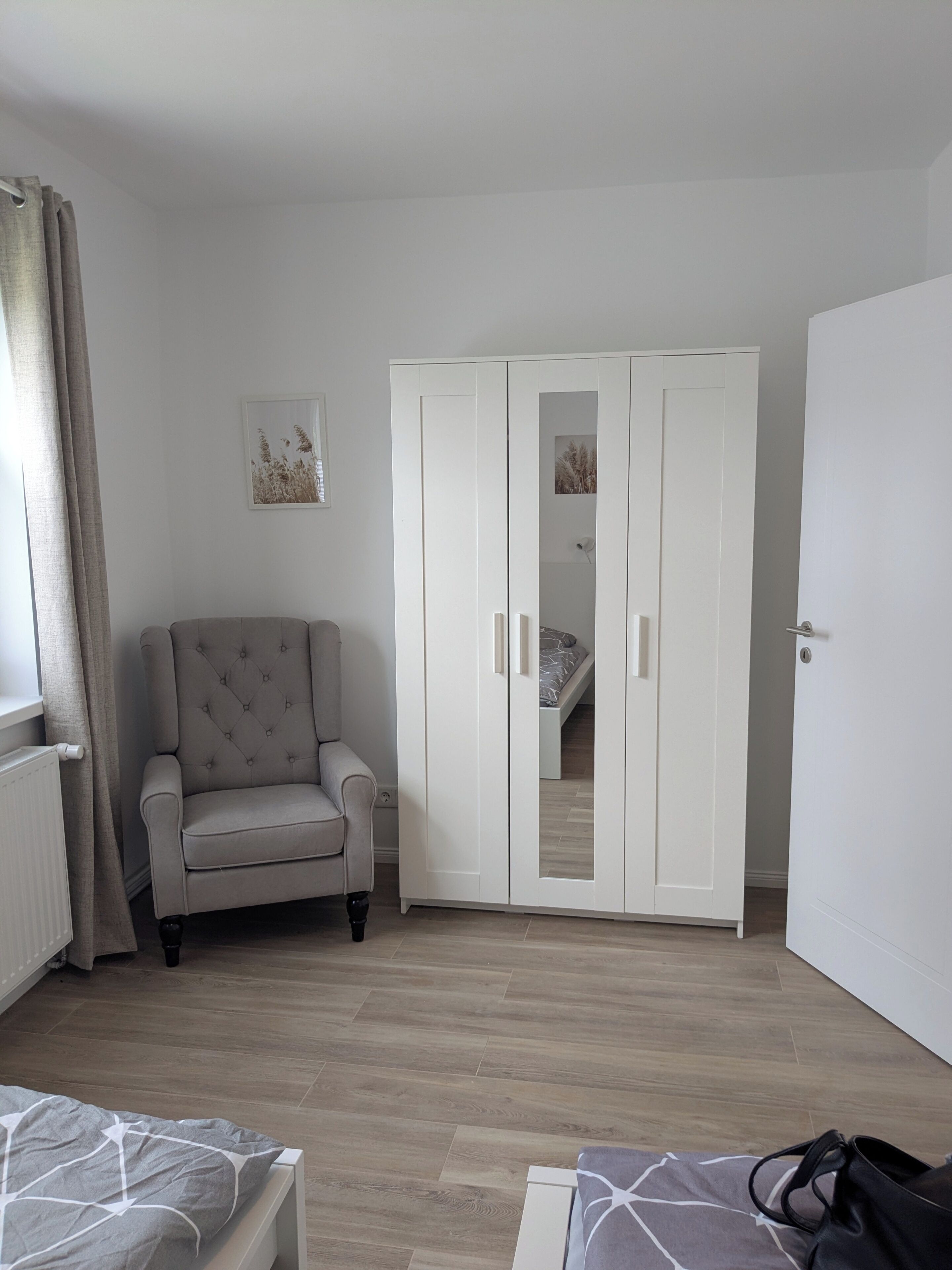 Un dormitorio con cama, armario, silla y radiador.