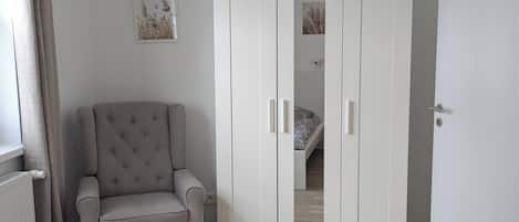 Un dormitorio con cama, armario, silla y radiador.