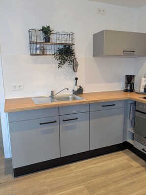 A modern kitchen with a wooden countertop, a stainless steel sink, grey cabinets, and a coffee machine. - Vacation Rental in Ranzig - Old but Gold (Tauche)