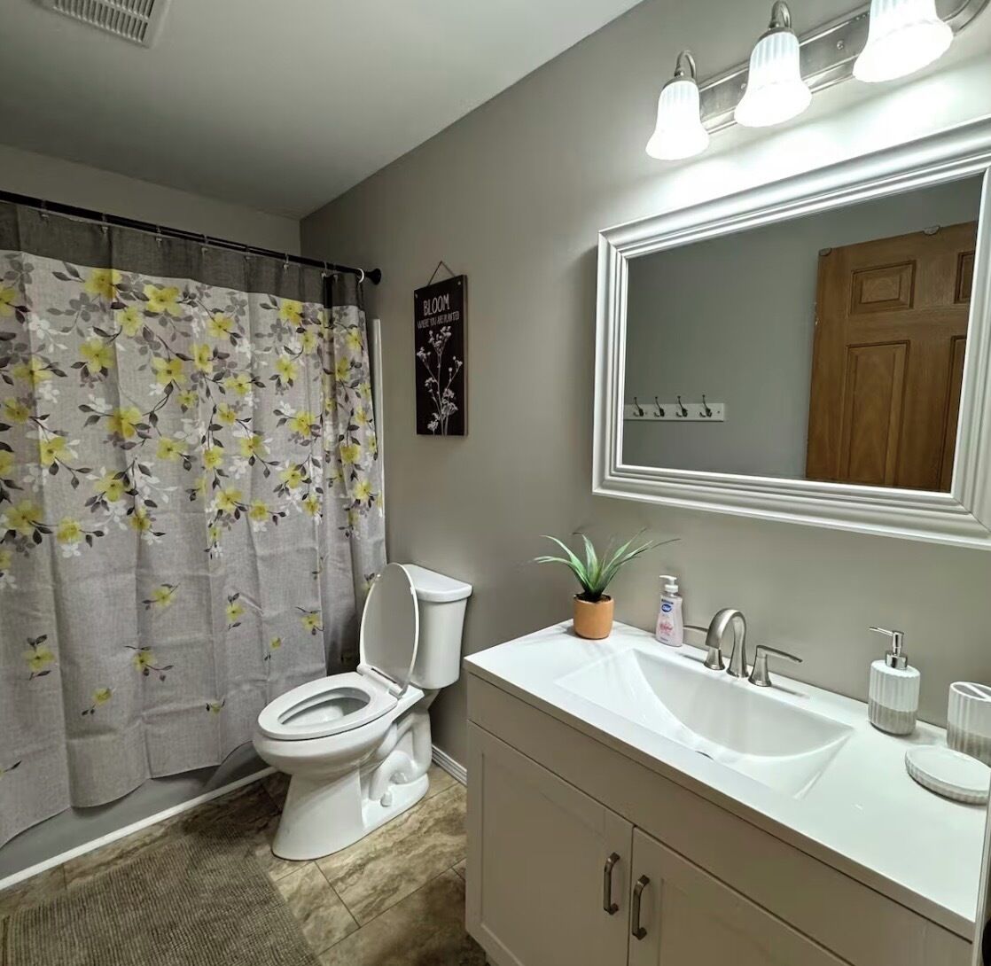 Un baño con inodoro, lavamanos, espejo y cortina de ducha.