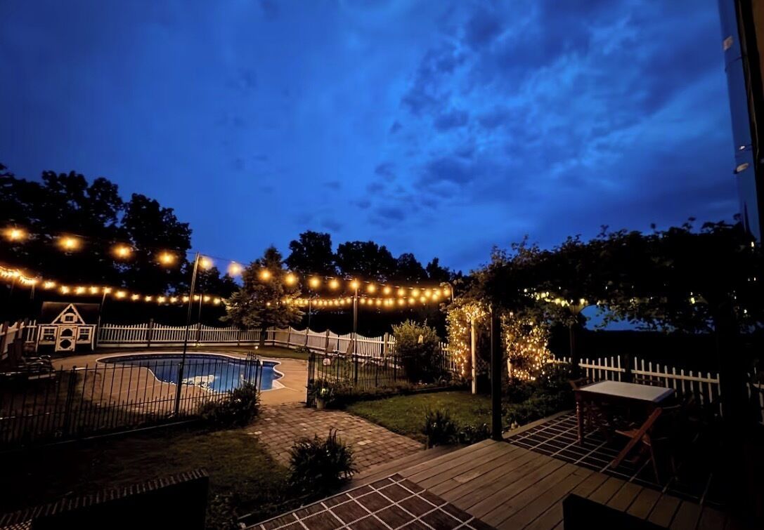 A backyard with a swimming pool, a wooden deck, and string lights.