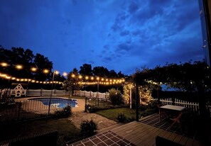 A backyard with a swimming pool, a wooden deck, and string lights.