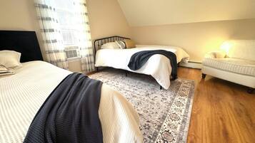 A bedroom with two beds, a patterned rug, a chair, and a window with curtains.