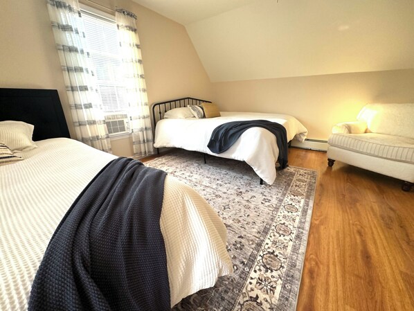 A bedroom with two beds, a patterned rug, a chair, and a window with curtains.