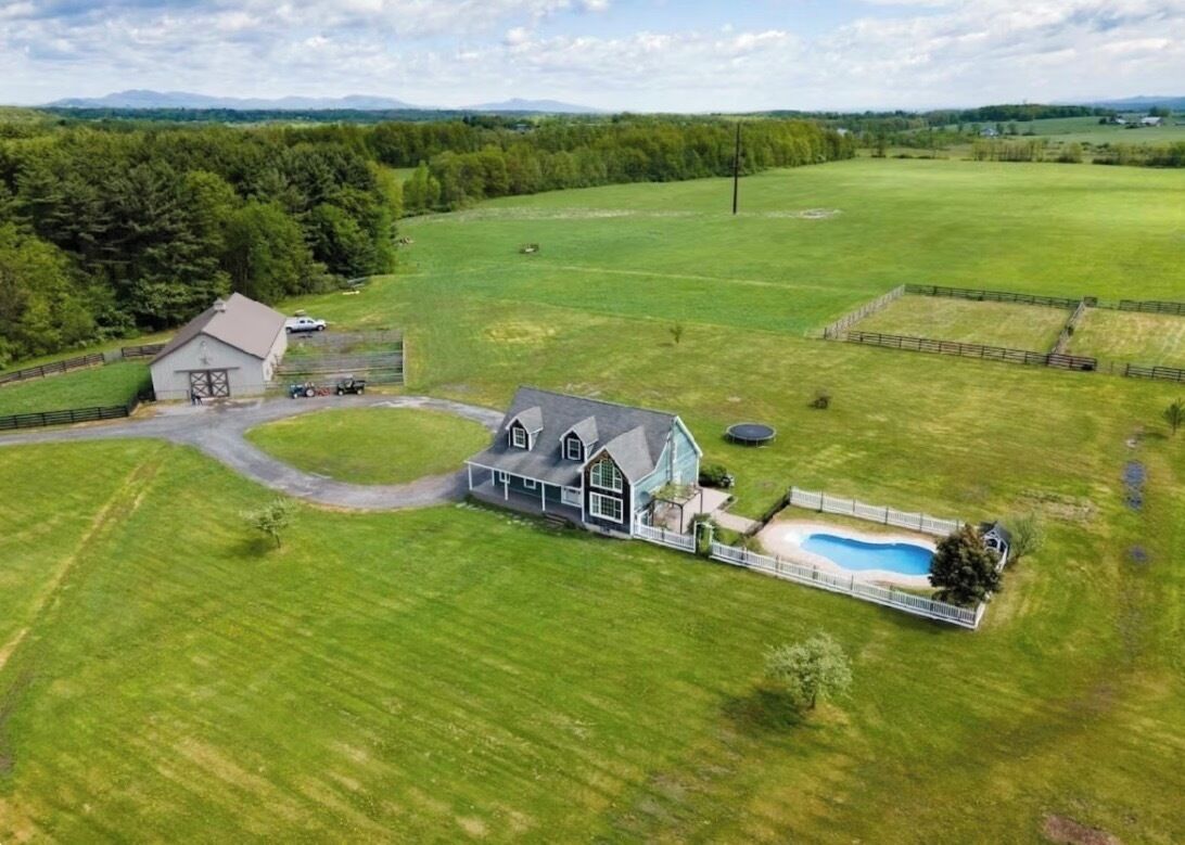 Une grande maison avec une grange, entourée de vastes champs verdoyants et dotée d’une piscine.