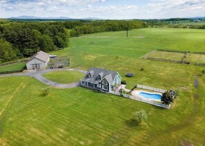 A large house with a barn, surrounded by expansive green fields and a swimming pool.