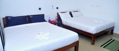 Two single beds with wooden frames and white linens, a bedside table with a bottle and a box, and a wall-mounted thermostat.