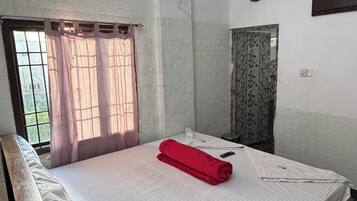 A room with a bed, a ceiling fan, a window with curtains, a clock on the wall, and a door with a patterned curtain.