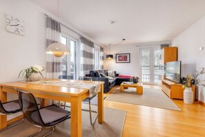 A modern living room with a wooden dining table, black chairs, a sofa, a coffee table, and a TV. - "Island Pearl" in the Margarete Residence (Binz)