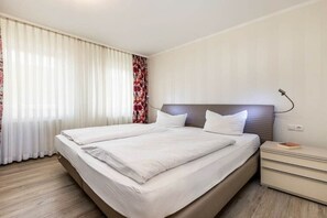 A hotel room with a large bed, a bedside table, and a window with curtains. - Seaside joy at the Baltic Sea House (Binz)