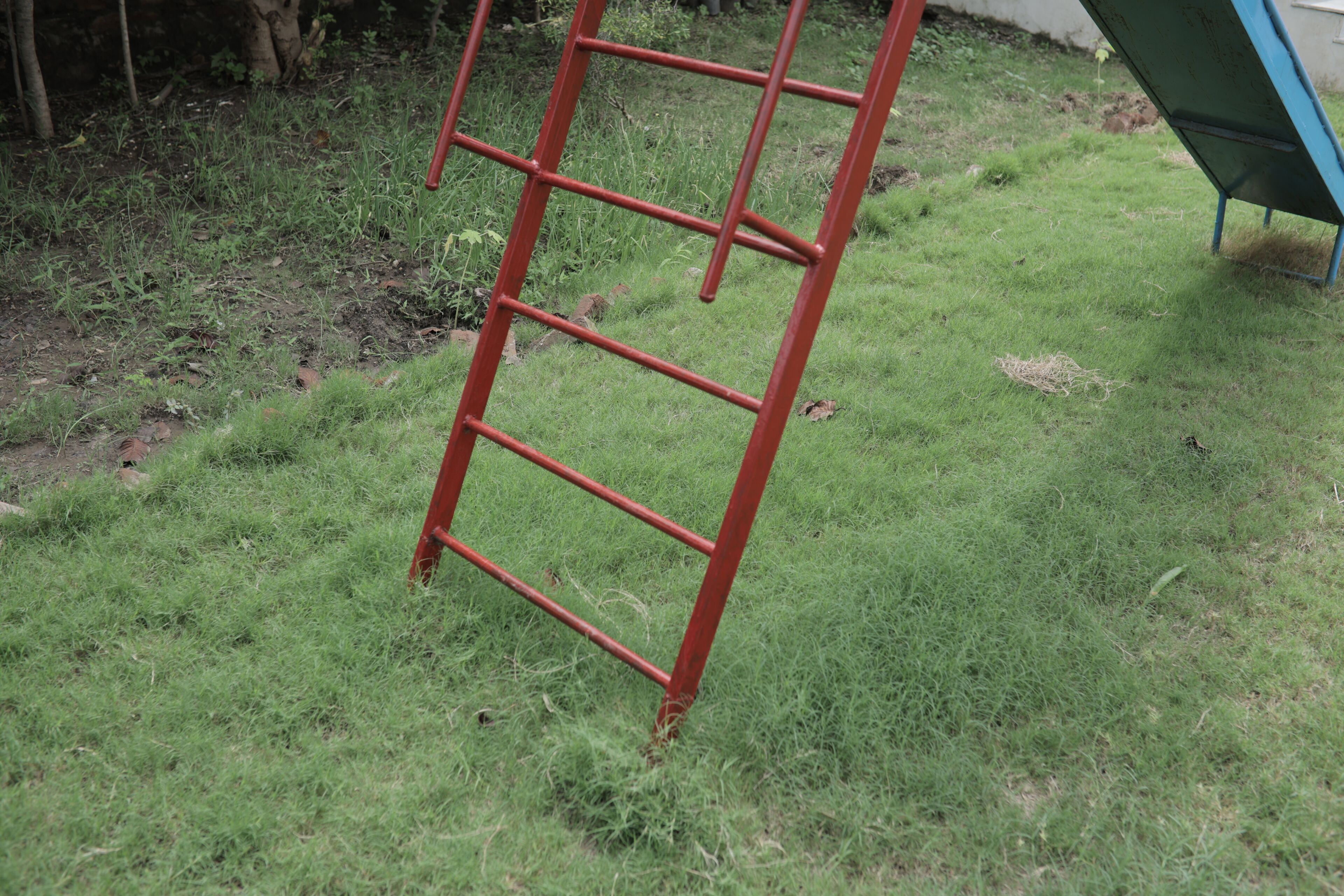 Een rode metalen ladder die tegen een gazon staat.