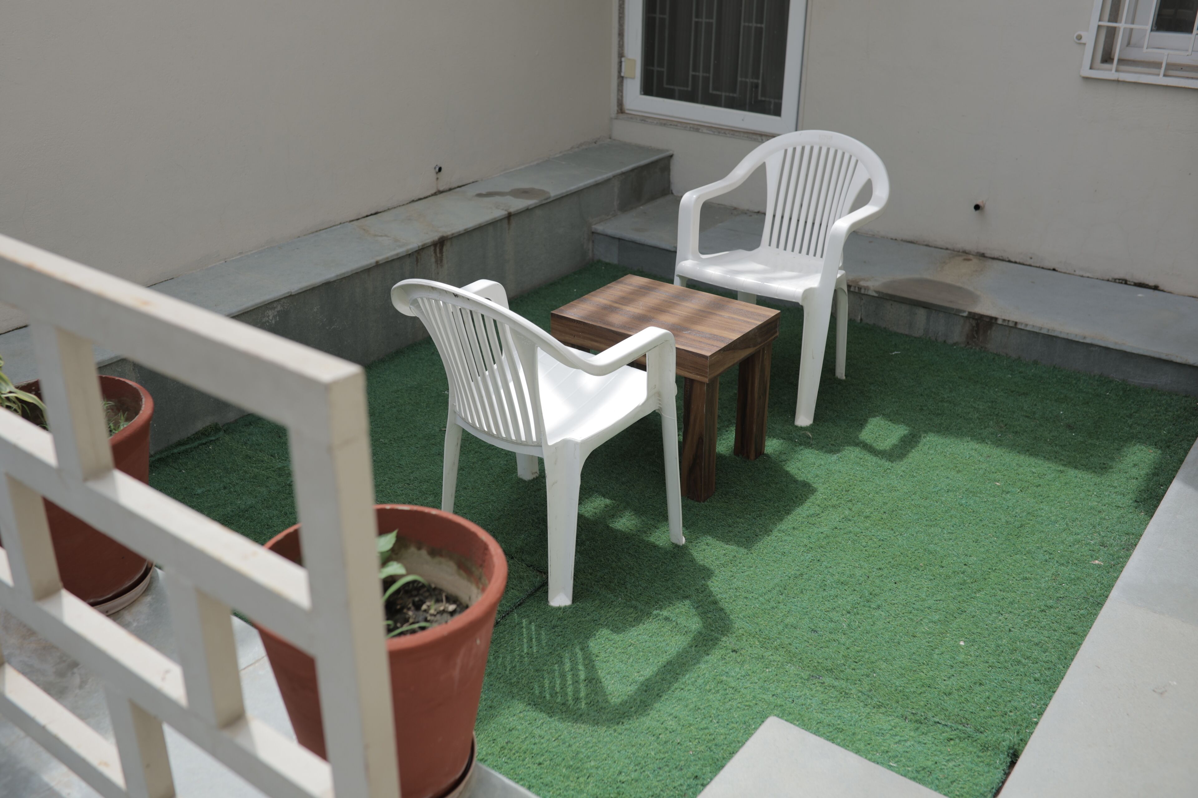Een klein buitgedeelte met twee witte plastic stoelen en een houten tafel, omringd door kunstgras.