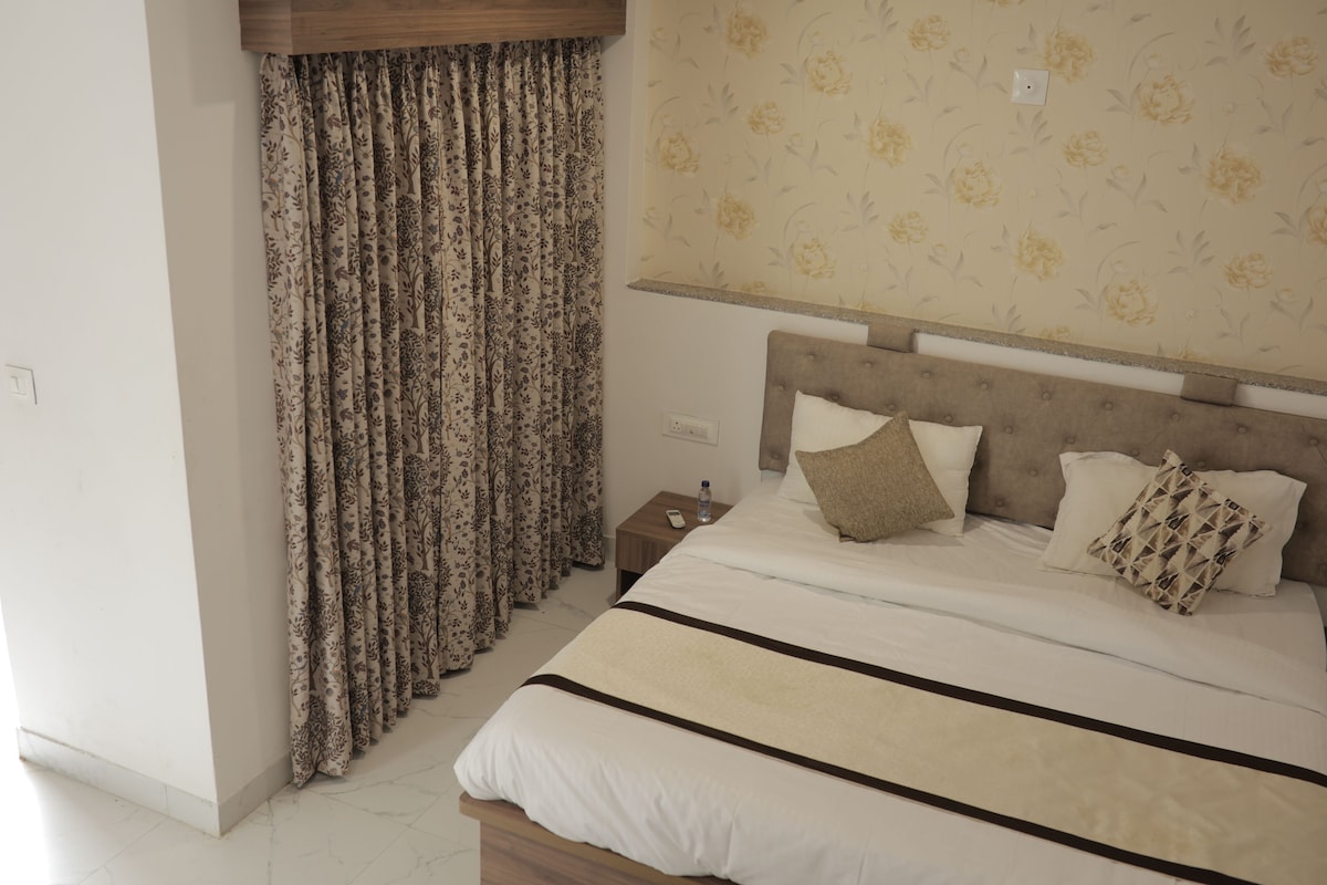 Quarto com cama, mesa de cabeceira e cortinas.