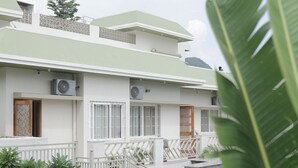 Un moderno edificio de dos pisos con techo plano, unidades de aire acondicionado y un pequeño jardín con césped y plantas.