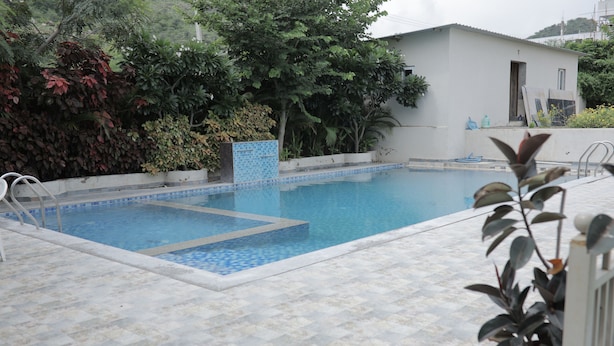 Piscina com bordas azulejadas, cercada por vegetação e um edif ício ao fundo.