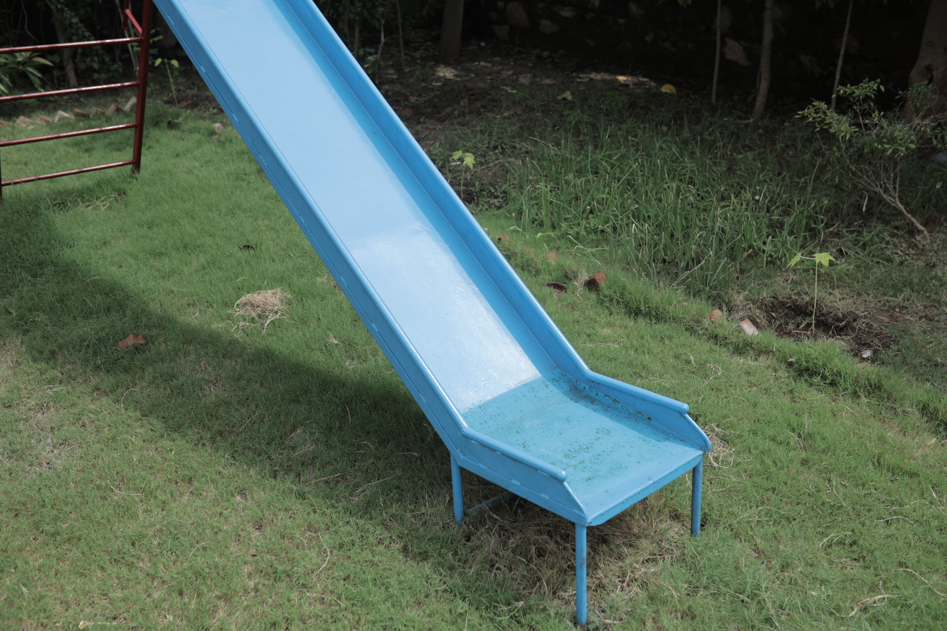 A blue slide in a grassy area with a metal structure in the background.