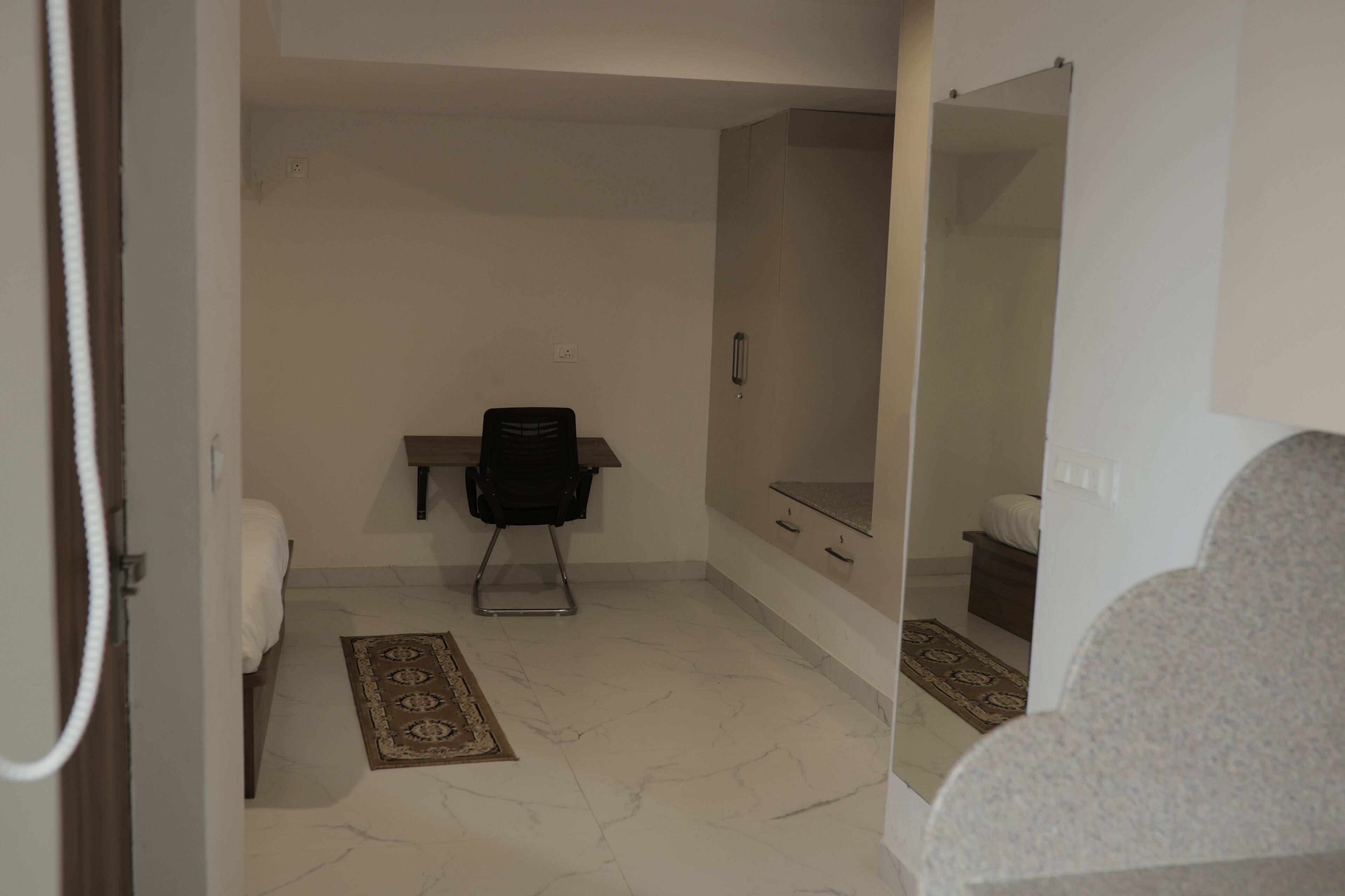 A hotel room with a bed, a desk, a chair, a mirror, and a bathroom.