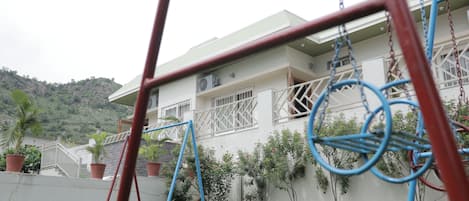 Edifício residencial com varanda, vasos de plantas e balanço em primeiro plano.