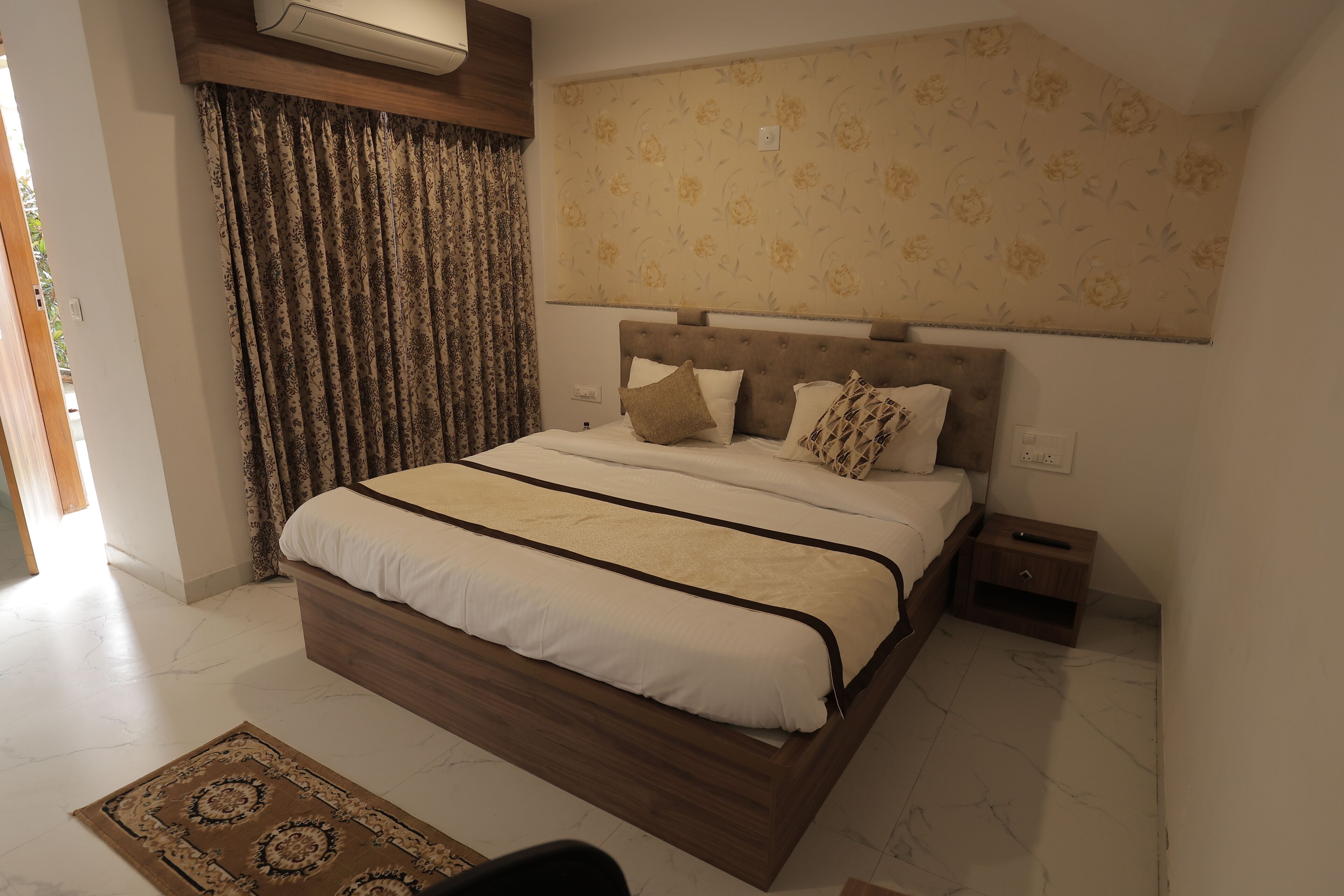 A bedroom with a bed, curtains, a nightstand, and a wall-mounted air conditioner.