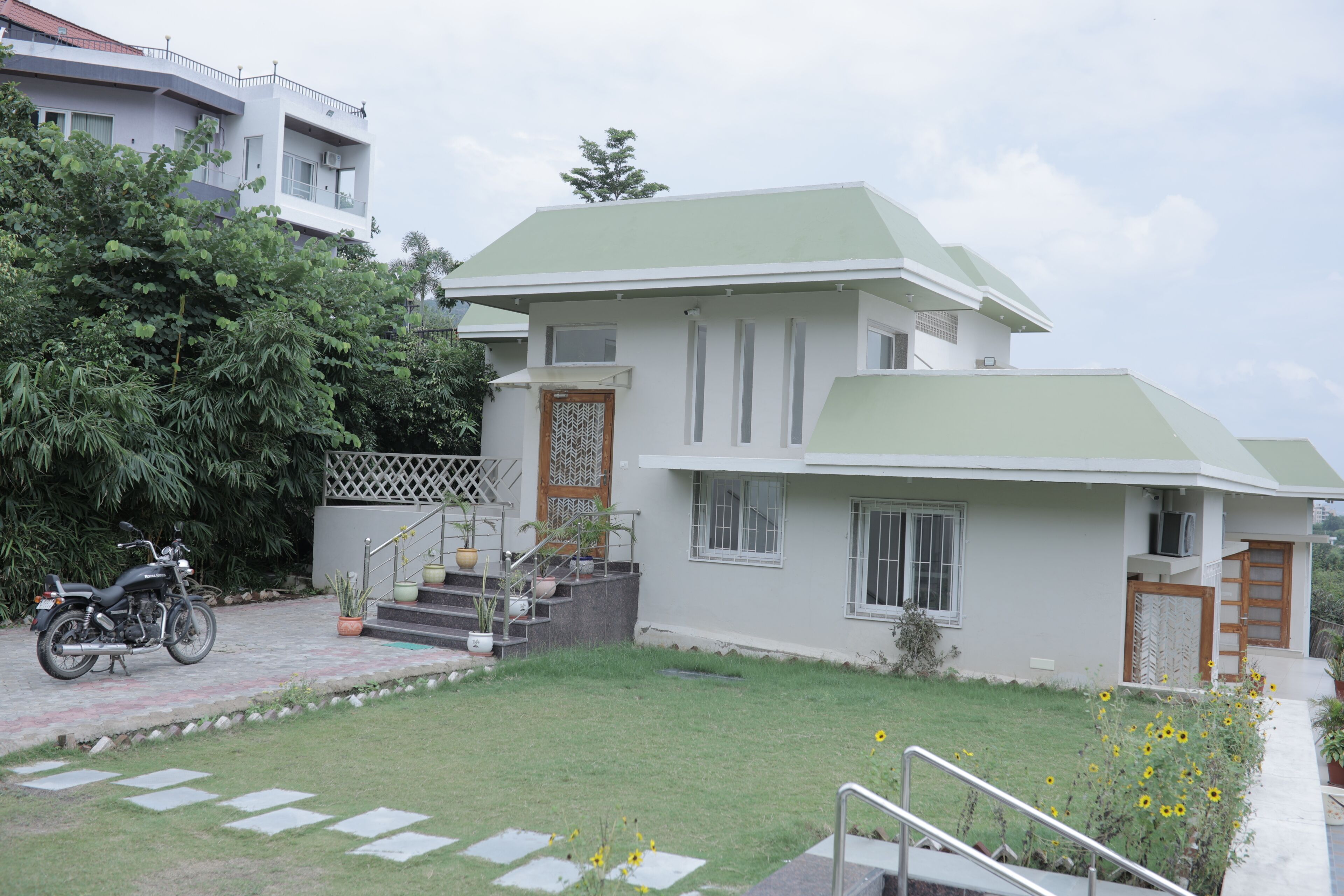 A two-story building with a green roof, a staircase leading to the entrance, and a motorcycle parked in front.